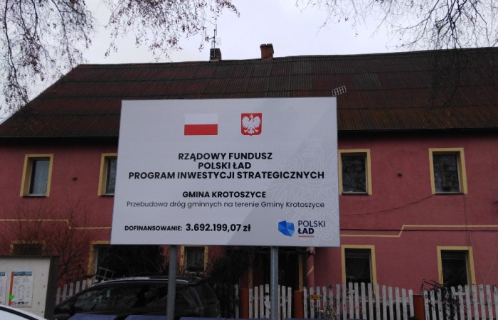 Zdjęcie przedstawia tablice informującą o dofinanosowaniu przebudowy dróg w gminie Krotosztce w ramach programu Polski Ład