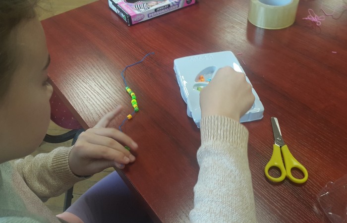 Dziewczynka tworzy branzoletkę z koralików